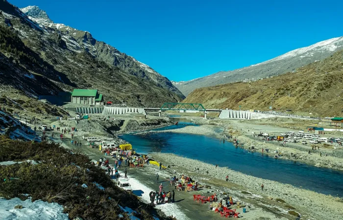 alt="Tourists enjoying riverbank near snow-capped mountains in Lachung, Sikkim">